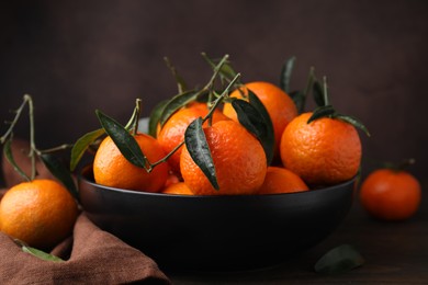 Photo of Fresh ripe tangerines with green leaves in bowl on table, closeup