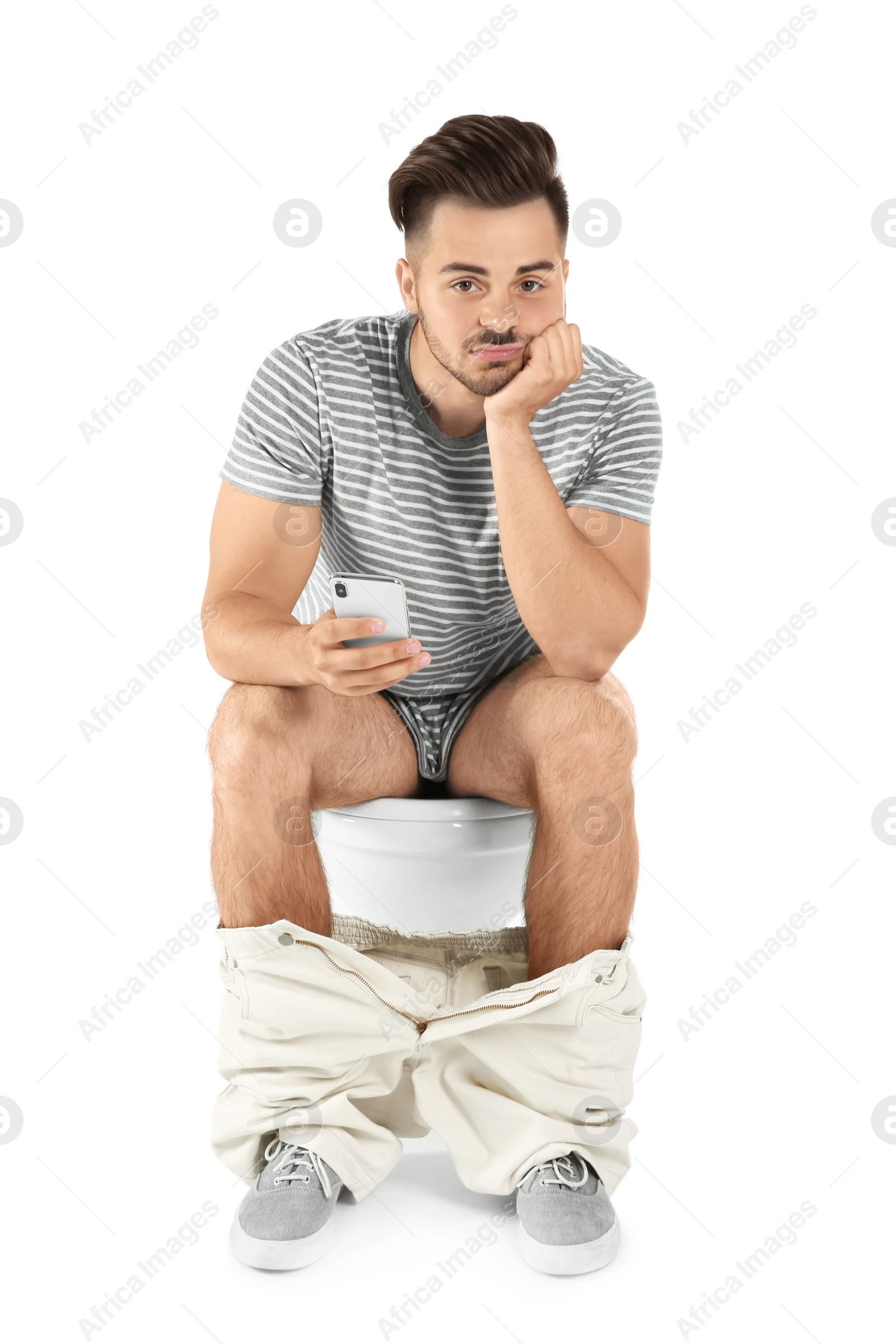 Photo of Young man using mobile phone while sitting on toilet bowl. Isolated on white