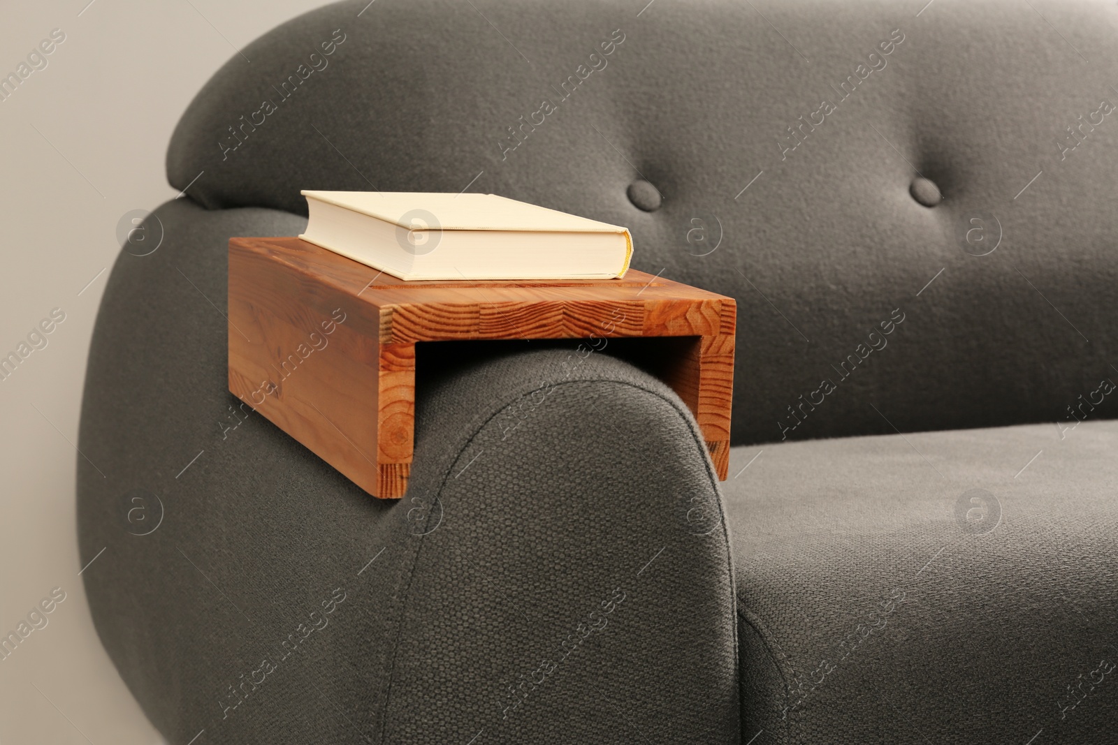 Photo of Book on sofa with wooden armrest table in room. Interior element