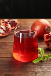 Photo of Tasty pomegranate juice in glass and fresh fruits on wooden table, closeup