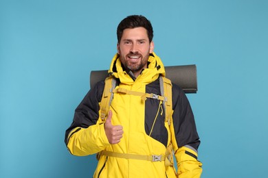 Photo of Happy man with backpack showing thumb up on light blue background. Active tourism