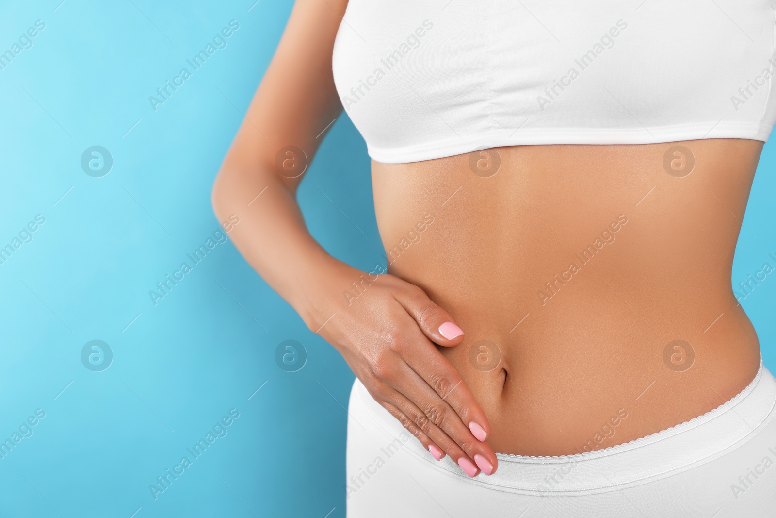 Photo of Woman in underwear touching her belly on light blue background, closeup. Healthy stomach