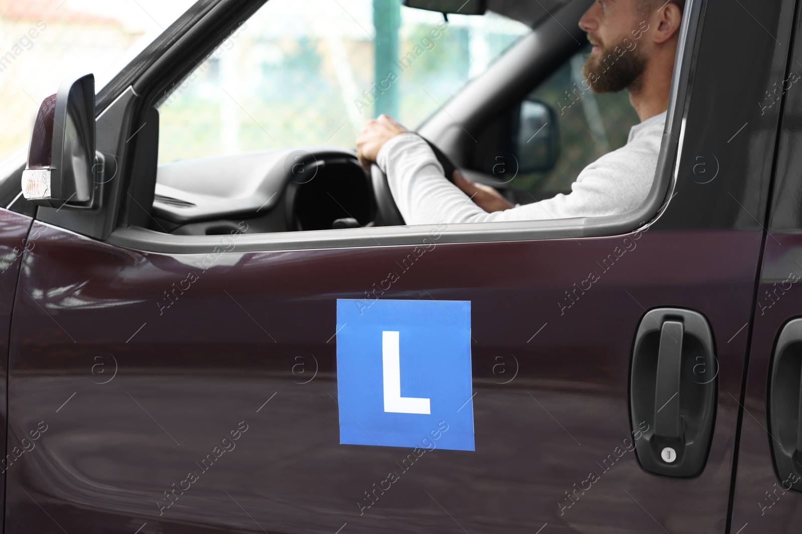 Photo of Learner driver driving car with L-plate, view from outside. Driving school