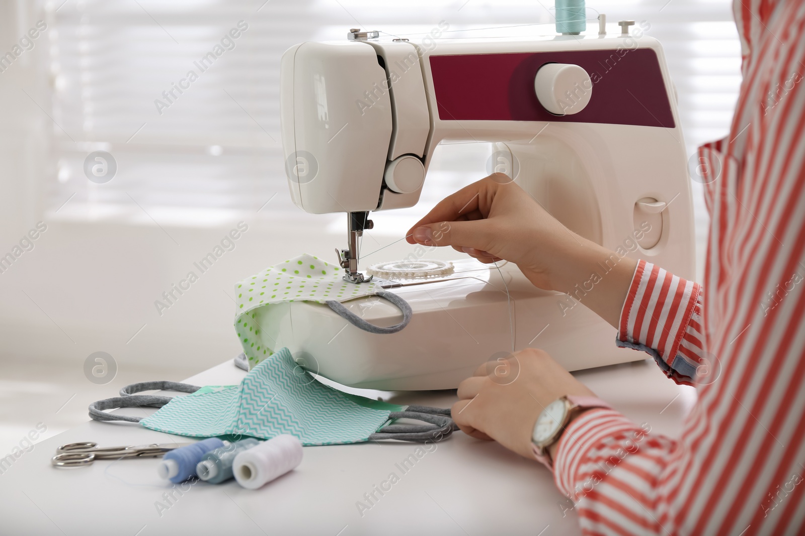 Photo of Woman making cloth mask with sewing machine at white table, closeup