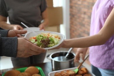 Photo of Poor man receiving food from volunteer indoors, closeup