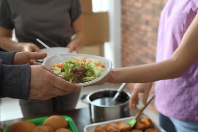 Poor man receiving food from volunteer indoors, closeup