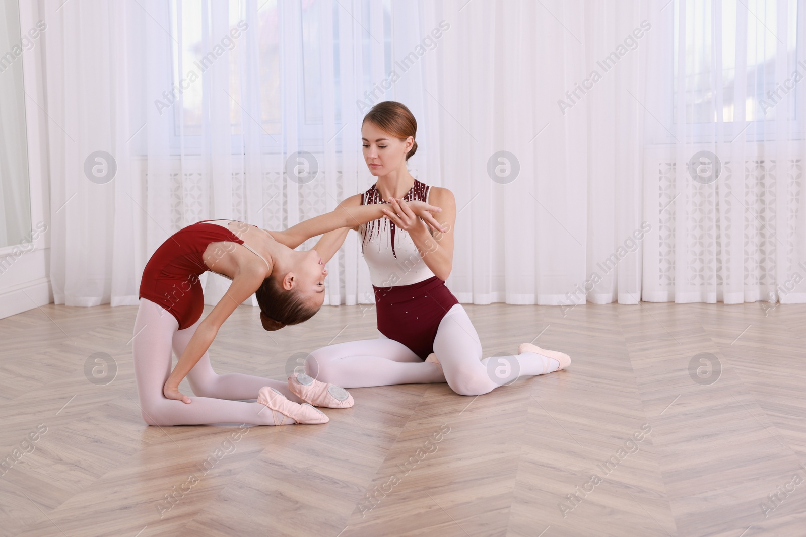 Photo of Ballet teacher helping little girl to stretch on floor in dance studio. Space for text