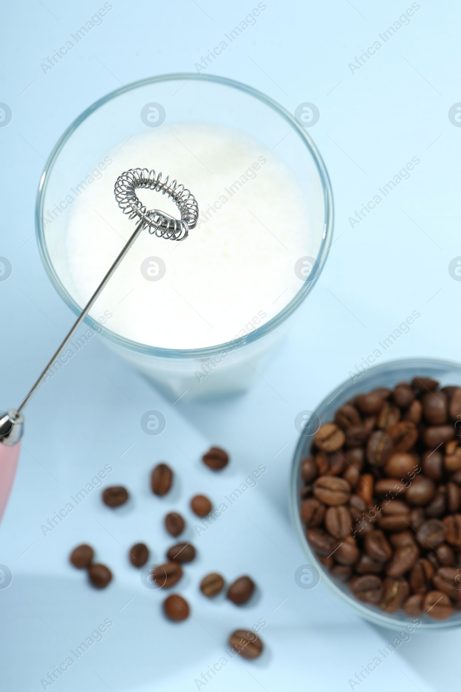 Photo of Mini mixer (milk frother), whipped milk and coffee beans in glasses on light blue background, flat lay