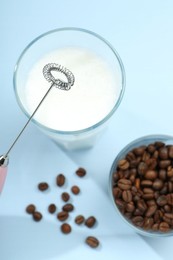 Mini mixer (milk frother), whipped milk and coffee beans in glasses on light blue background, flat lay