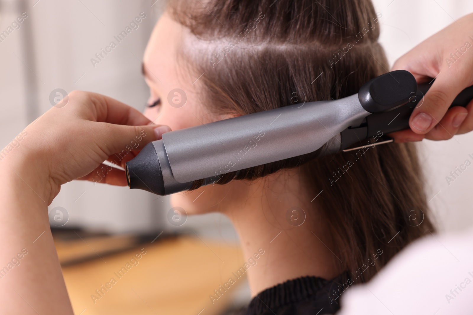 Photo of Hairdresser curling woman's hair with iron in salon, selective focus