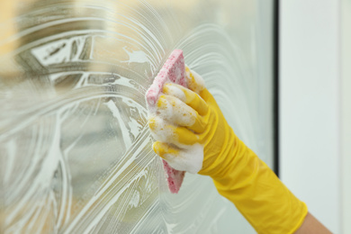 Woman cleaning window with sponge at home, closeup