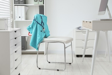Photo of Turquoise medical uniform and stethoscope hanging on chair in clinic