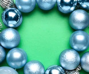 Frame of shiny Christmas balls and fir branches on green background, flat lay. Space for text