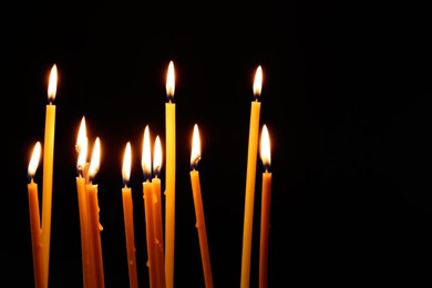 Many burning church candles on dark background. Space for text