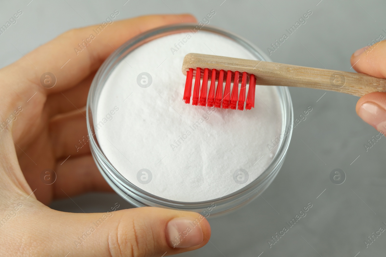 Photo of Woman with toothbrush and bowl of baking soda at grey table, closeup