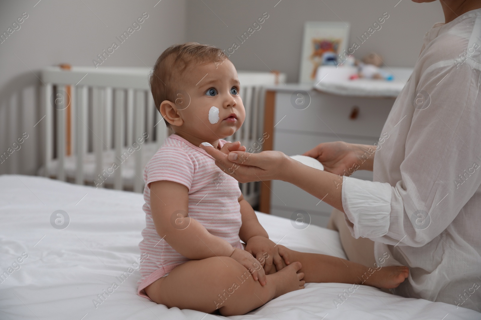 Photo of Mother applying moisturizing cream on her little baby at home, closeup