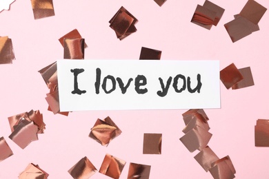 Card with text I Love You and shiny glitter on pink background, flat lay