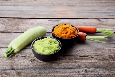 Photo of Tasty puree in bowls, zucchini and carrots on wooden table