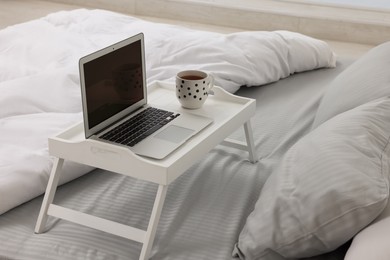 Photo of White tray table with laptop and cup of drink on bed