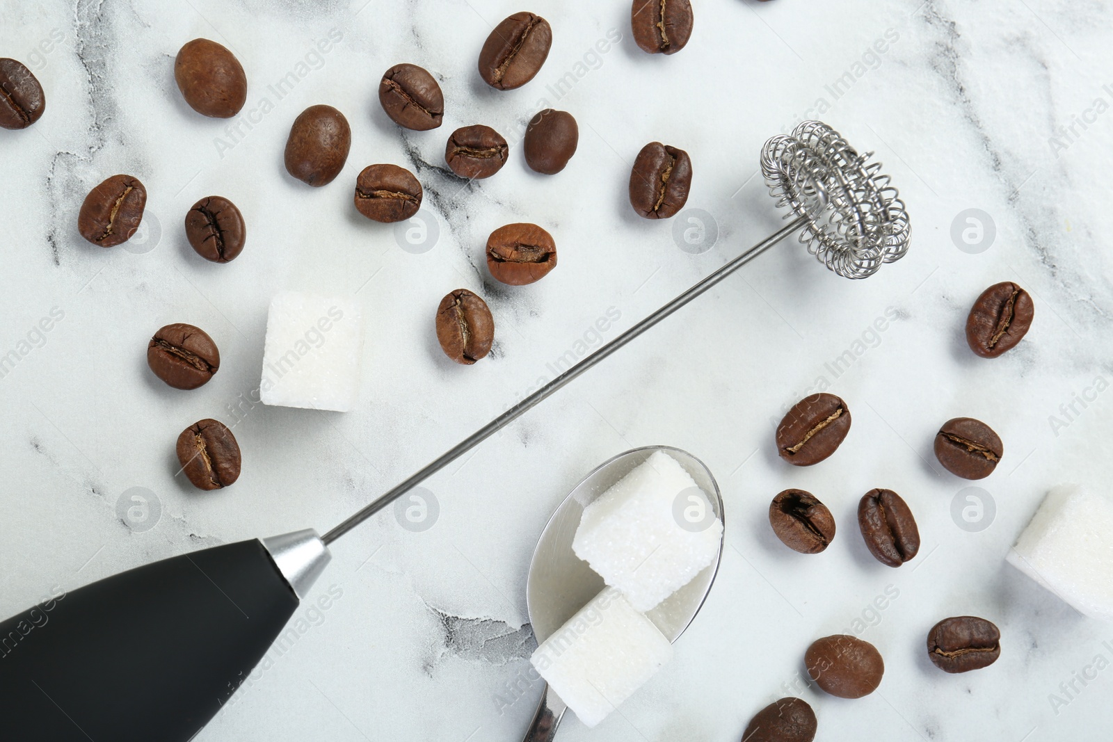 Photo of Black milk frother wand, sugar cubes and coffee beans on white marble table, flat lay