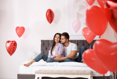 Lovely young couple in bedroom decorated with heart shaped balloons. Valentine's day celebration