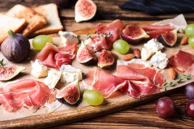 Photo of Ripe figs and prosciutto served on wooden table, closeup