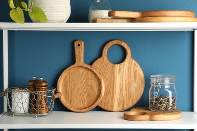 Wooden cutting boards, kitchen utensils and dry tea on shelving unit near blue wall