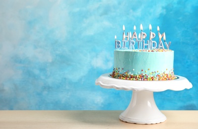 Fresh delicious birthday cake with candles on stand against color background. Space for text