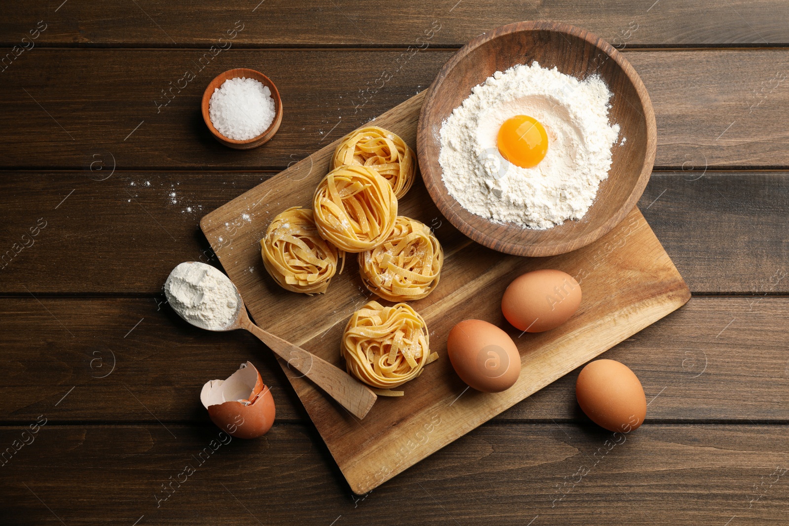 Photo of Uncooked homemade pasta and ingredients on wooden table, flat lay