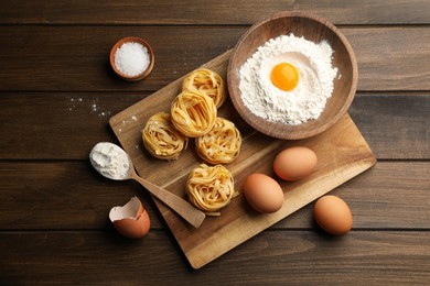 Photo of Uncooked homemade pasta and ingredients on wooden table, flat lay