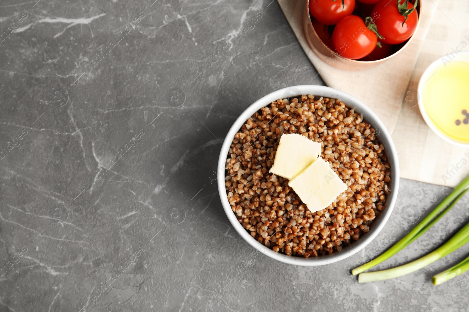 Photo of Flat lay composition with bowl of buckwheat porridge on grey marble table. Space for text