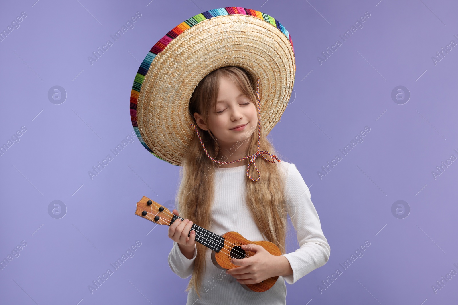 Photo of Cute girl in Mexican sombrero hat playing ukulele on purple background