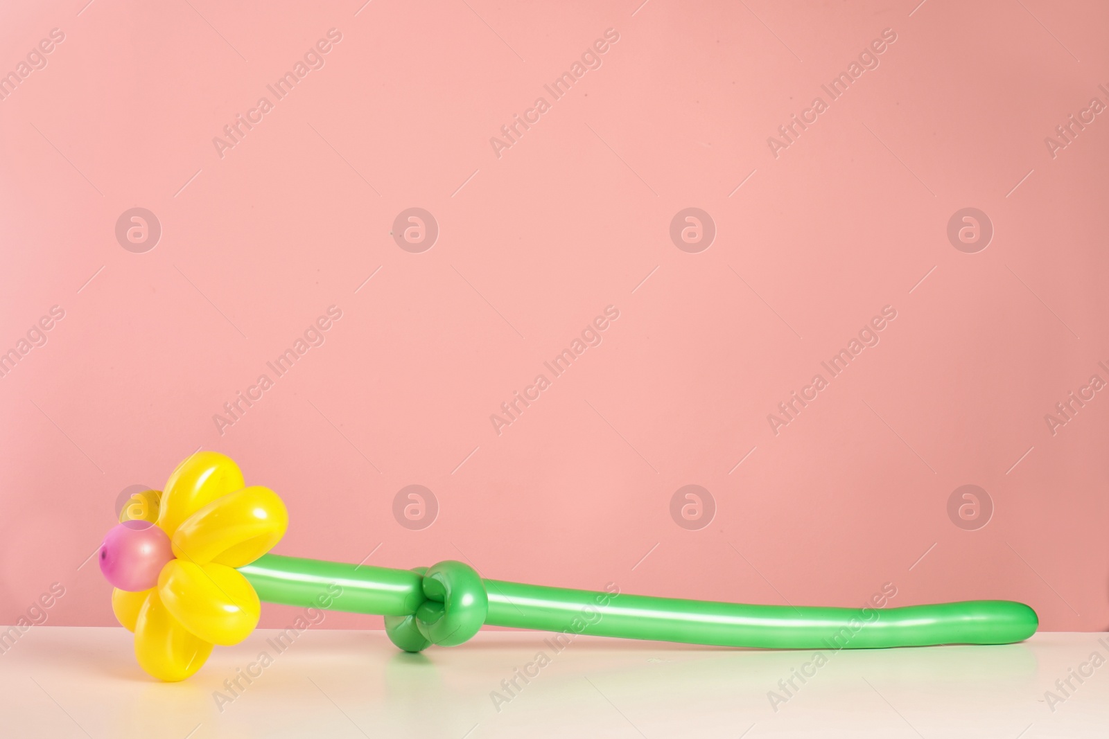 Photo of Flower figure made of modelling balloon on table against color background. Space for text
