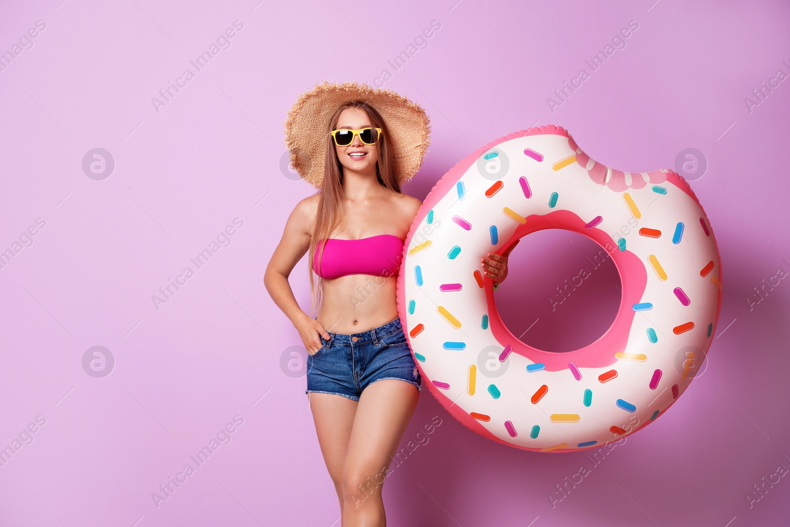 Photo of Beautiful young woman in beachwear and hat with inflatable ring on color background