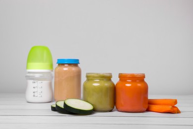 Photo of Healthy baby food, bottle with milk and fresh vegetables on white wooden table