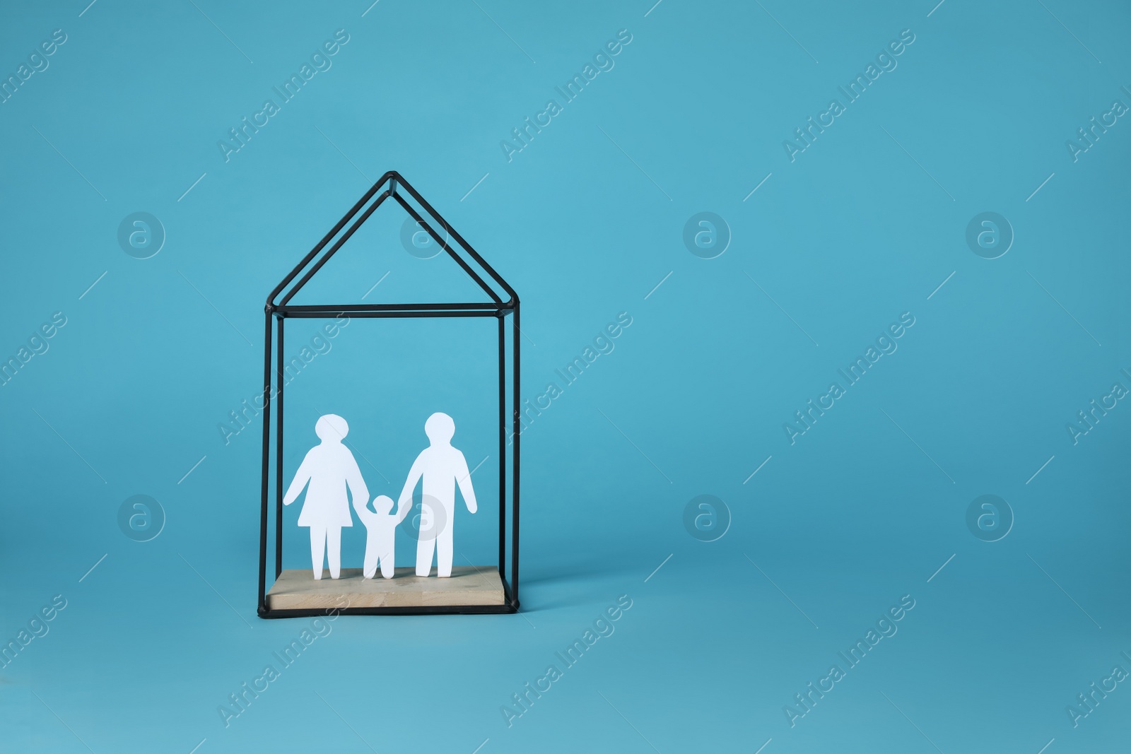 Photo of Paper cutout of parents with their child in house shaped metal stand on light blue background, space for text. Family Day