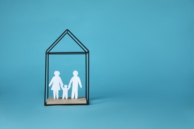 Photo of Paper cutout of parents with their child in house shaped metal stand on light blue background, space for text. Family Day