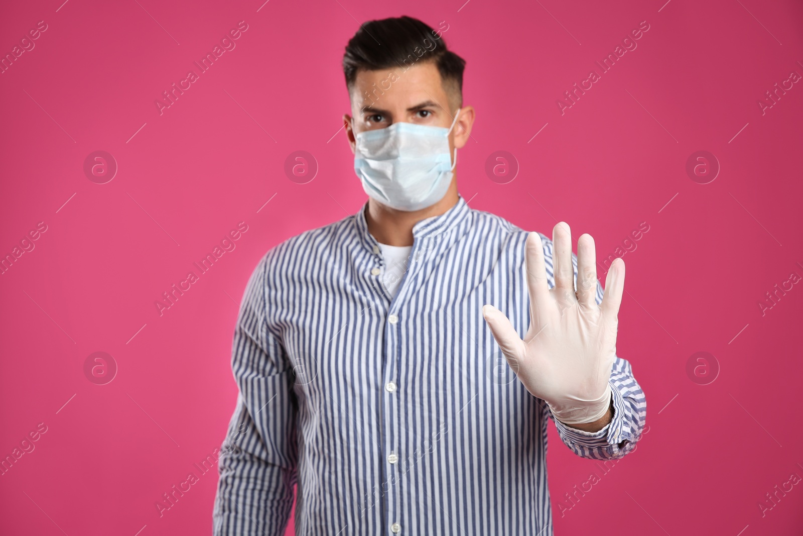 Photo of Man in protective face mask and medical gloves showing stop gesture against pink background, focus on hand