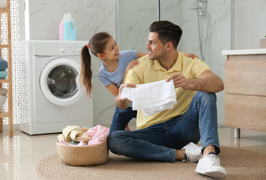 Photo of Father and little daughter with clean laundry in bathroom