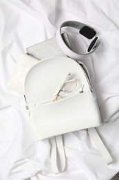 Photo of Stylish urban backpack with different items on white fabric, flat lay