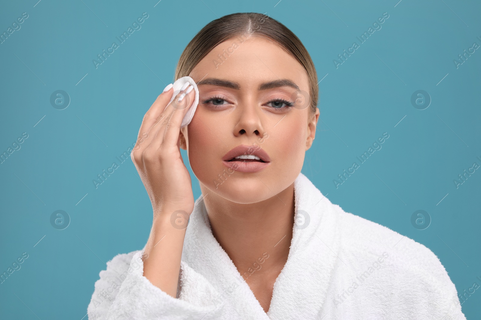 Photo of Beautiful woman removing makeup with cotton pad on light blue background