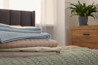 Photo of Stack of different folded blankets on bed in room, space for text. Home textile