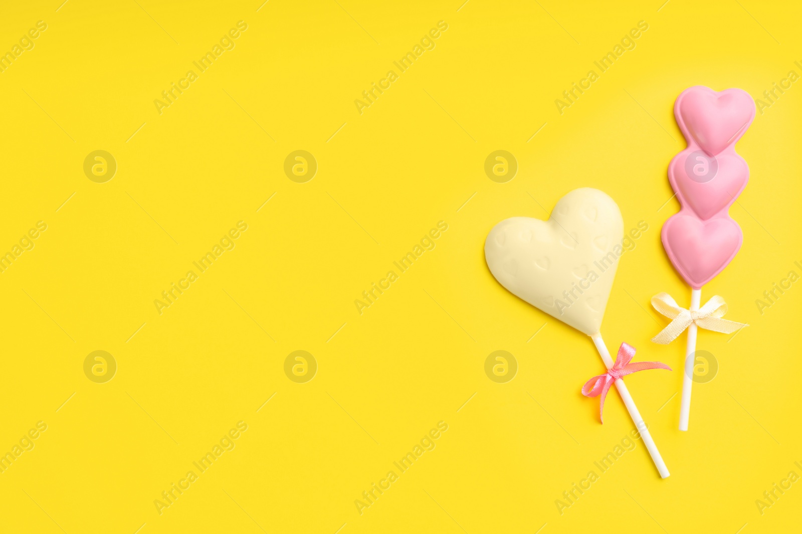 Photo of Different chocolate heart shaped lollipops on yellow background, flat lay. Space for text