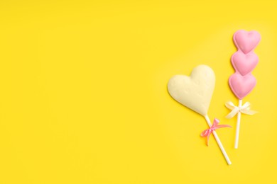 Photo of Different chocolate heart shaped lollipops on yellow background, flat lay. Space for text