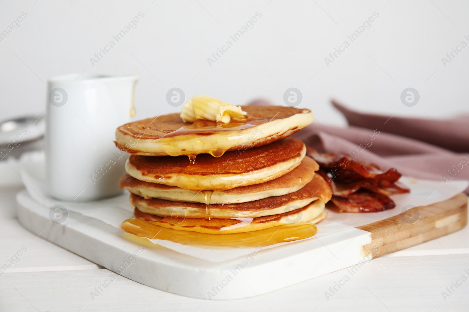 Photo of Delicious pancakes with maple syrup, butter and fried bacon on white wooden table