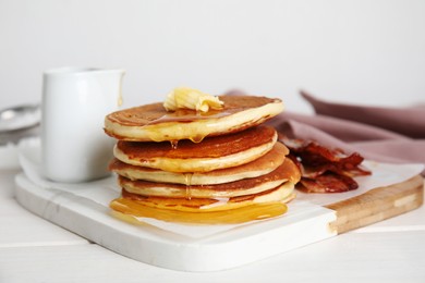 Photo of Delicious pancakes with maple syrup, butter and fried bacon on white wooden table