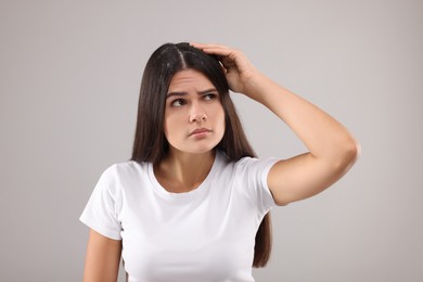 Photo of Emotional woman examining her hair and scalp on grey background. Dandruff problem