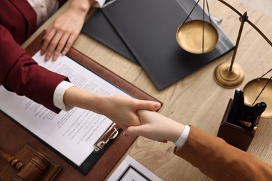 Notary shaking hands with client at wooden table, closeup