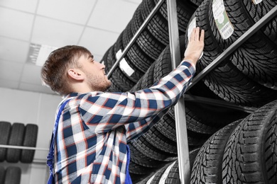 Young male mechanic with car tires in automobile service center