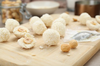 Photo of Delicious candies with coconut flakes and hazelnut on wooden board, closeup